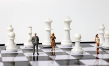 Satranç tahtasında ayakta duran minyatür insanlar ve satranç taşları.