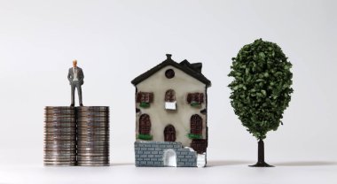 Minyatür bir ev ve minyatür bir ağacın yanında madeni paraların üzerinde duran minyatür bir adam..