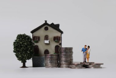 Minyatür ağaç ve minyatür evi olan madeni paraların üzerinde minyatür bir çift..