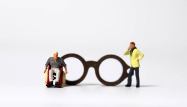 Tekerlekli sandalyede minyatür bir adam ve minyatür bir adamın tahta minyatür bir bardağın önünde durması..