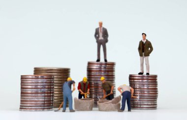 Madeni para yığınının üzerinde duran minyatür adamlar ve altında çalışan minyatür adamlar. Gelir açığı kavramı.