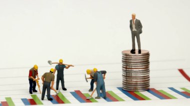 Takım elbiseli bir adam, bir yığın madeni paranın üzerinde, bir grafiğe ve bir inşaat sahasında minyatür işçilere karşı duruyordu..