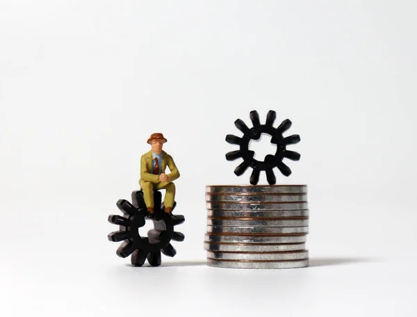 Cogwheel Pile Coins Alongside Miniature Man Sitting Cogwheel — Stock Photo, Image