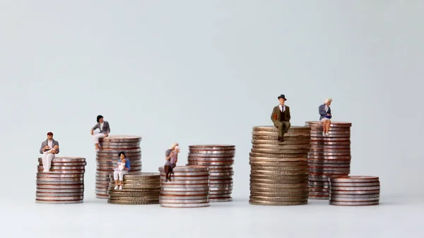 Miniature people standing on piles of different heights of coins. The concept of the income gap between individuals that is not addressed.