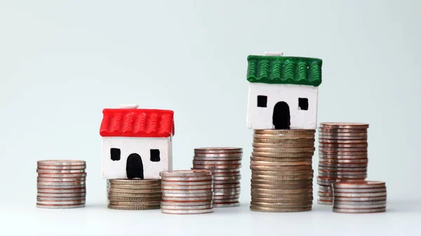 A miniature house on a pile of different heights of coins. Household income gap concept.