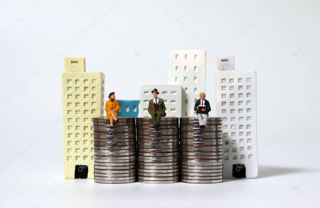 Miniature people sitting on piles of coins and miniature buildings.