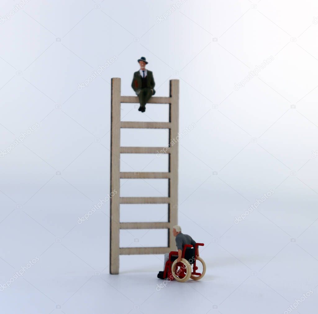 A miniature man sitting on a wooden ladder and a miniature man in a wheelchair.