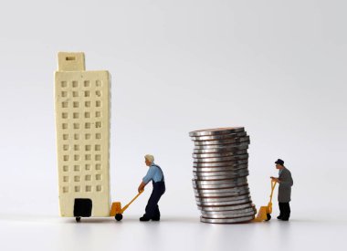 Minyatür bir binayı el arabasına taşıyan minyatür bir adam ve bir araba dolusu madeni parayı taşıyan minyatür bir adam..