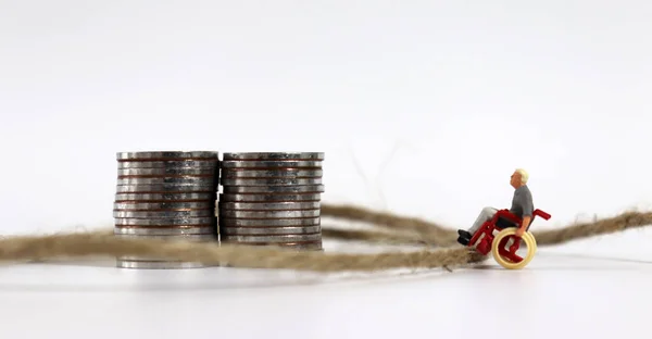 Een Miniatuurman Een Rolstoel Een Touw Met Een Stapel Munten — Stockfoto