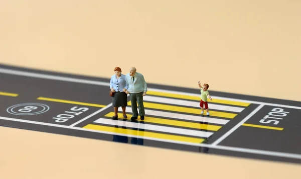 A miniature old couple and a miniature boy crossing a crosswalk.