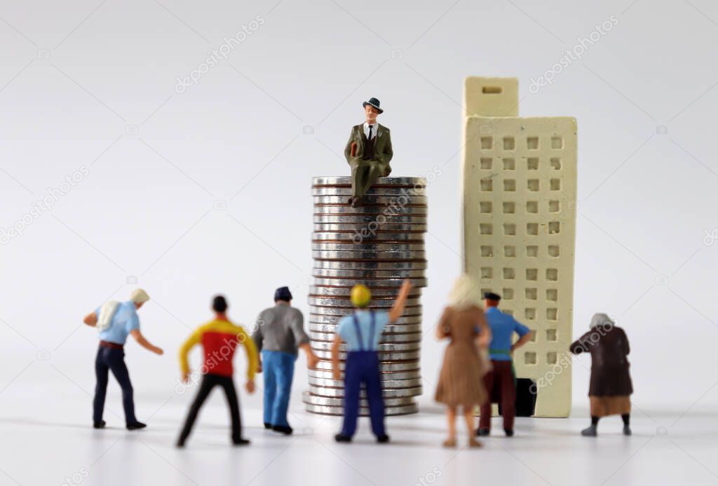 Numerous miniature people gathered in front of miniature buildings and piles of coins.