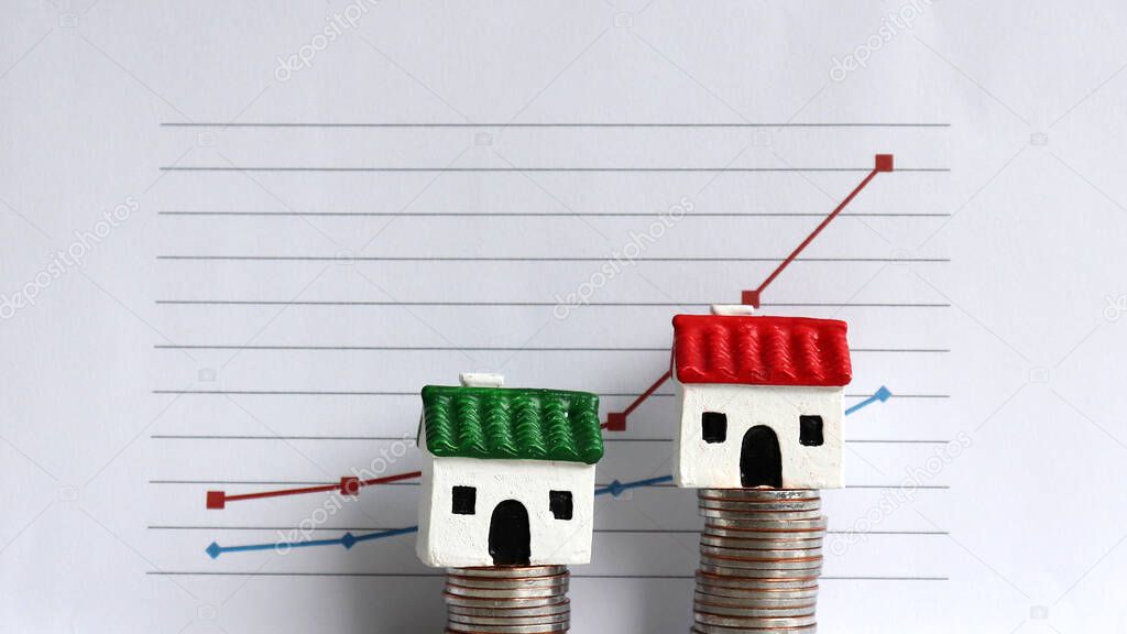 A miniature house on a pile of coins in front of a graph.
