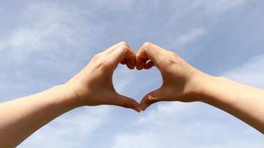 Bir kadının eli mavi bahar gökyüzüne kalp oluşturur..