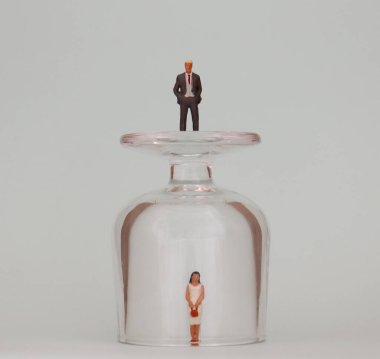 Cam bardakta minyatür bir kadın ve cam bardağın üstünde minyatür bir adam. Terfi eden kadınlar için görünmez engeller kavramı.