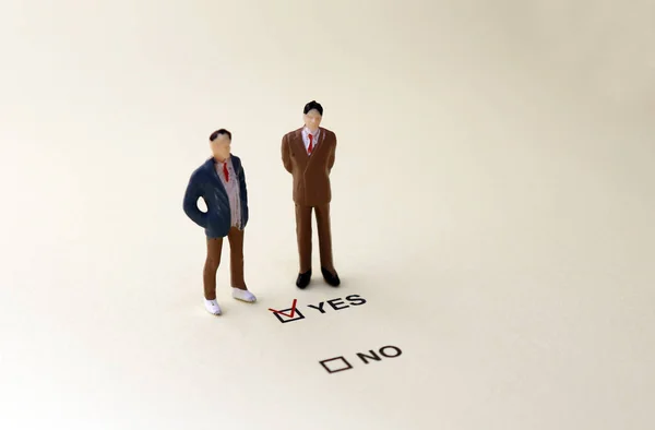 YES and NO check boxes with red check mark in the YES box. Two miniature men standing in front of the YES check box.