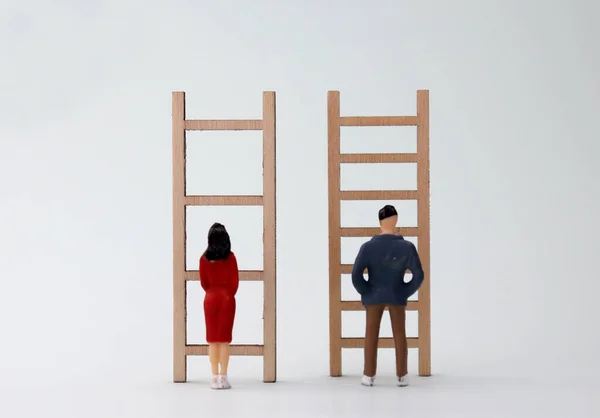 Miniature men and women standing in front of different ladders. The concept of discrimination of opportunities for men and women in society.