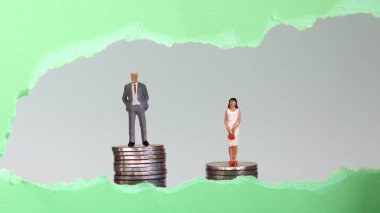 Yeşil yırtık kağıdın arkasında görünen madeni paraların üzerinde duran minyatür adam ve kadın. İş yerinde görünmez kadınlara karşı ayrımcılık kavramı.