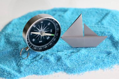 Gökyüzündeki pusula ve kağıt tekneler mavi kumlar. Seyahat planlama kavramları.