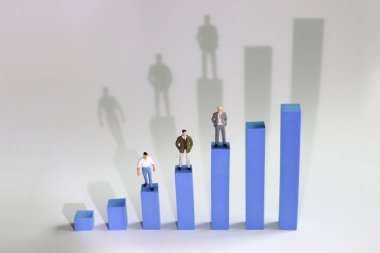 Üç minyatür adam mavi bir çubuk grafiğin üzerinde bir çubuğun üzerinde duruyor. Meslek tipine göre gelir açığı kavramı.