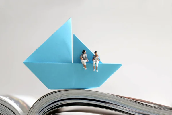 一对带着孩子坐在蓝色纸船上的迷你女同性恋夫妇在翻开的书页上 — 图库照片