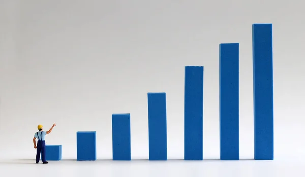 A miniature man pointing to a blue bar graph on a white background.