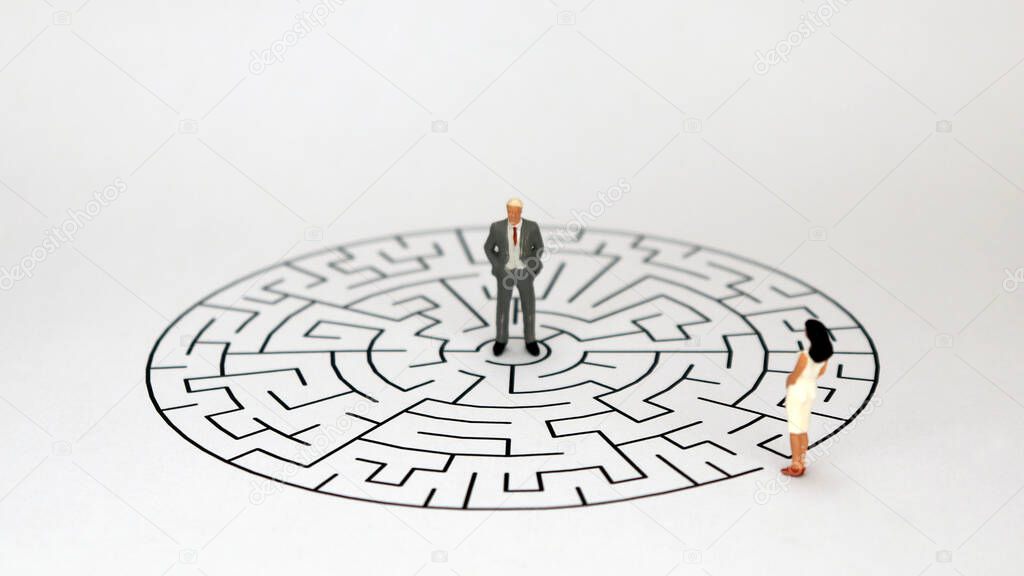 A miniature man standing in the middle of a round maze and a miniature woman standing at the entrance to the maze.
