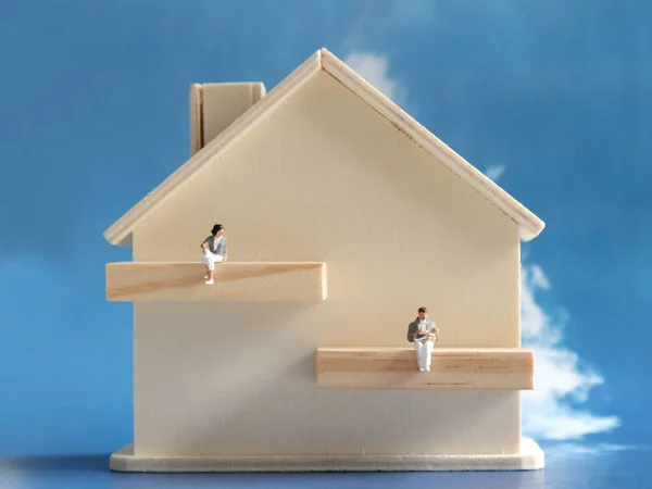 A miniature man and a miniature woman with a miniature wooden house. The concept of gender role change in the home.