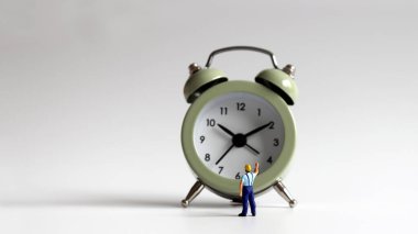 Minyatür bir adam çalar saati işaret ediyor..