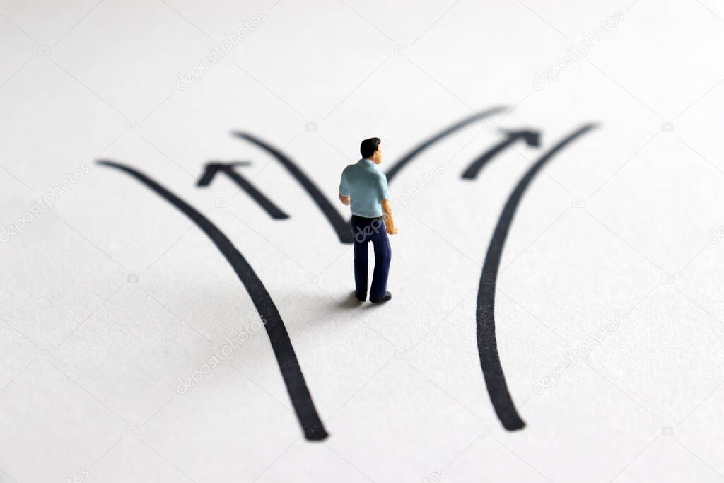A miniature man standing in front of two roads.