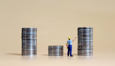 Madeni para yığınları arasında duran ve bozuk paraların tepesini gösteren minyatür bir adam..