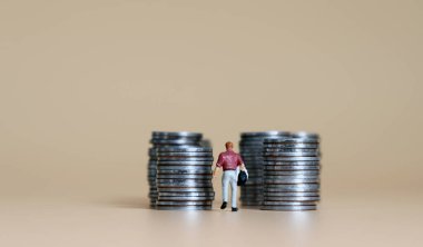 Gelir kavramı. Minyatür bir adam bozuk para yığınlarının arasında yürüyor..