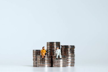 Minyatür yaşlı bir adam ve bozuk para yığınının üzerinde oturan minyatür yaşlı bir kadın. Yaşlanma için gelecek finansmana hazırlık kavramları.