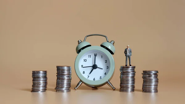 时间和经济价值的概念 一个小商人站在堆积如山的硬币和闹钟上 — 图库照片