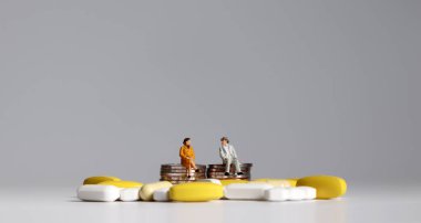 Minyatür yaşlı bir adam ve tabletlerle bozuk paraların üzerinde oturan minyatür bir yaşlı kadın..