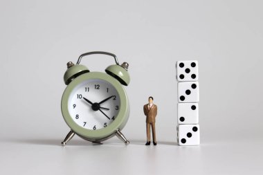 Çalar saatle zar arasında duran minyatür bir işadamı..