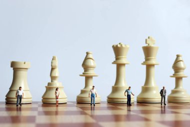 Satranç taşları ve satranç tahtasındaki minyatür insanlar..