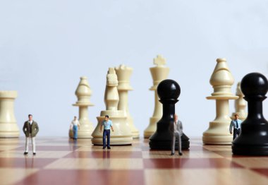 Satranç taşları ve satranç tahtasındaki minyatür insanlar..