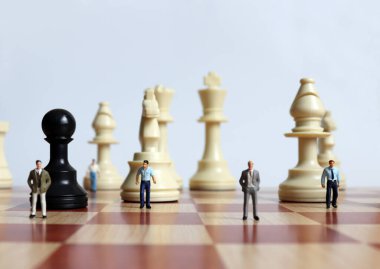 Satranç tahtasında satranç taşlarıyla duran minyatür insanlar..