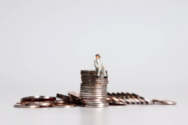 Bozuk paraların üzerinde oturan minyatür yaşlı bir adam..