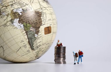 Dünyanın önünde madeni para yığınları olan minyatür turistler.