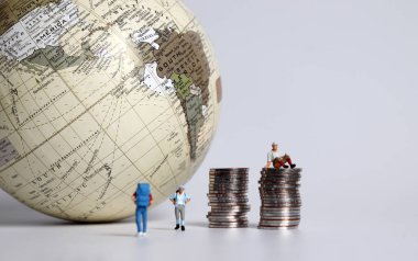 Küre ve para yığınları olan minyatür insanlar..