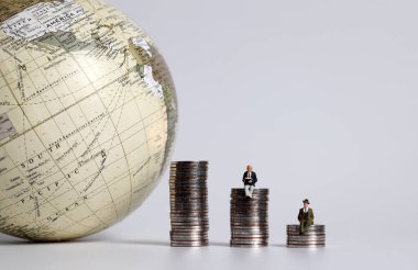 Küreyle yan yana üç madeni para yığını olan iki minyatür adam..