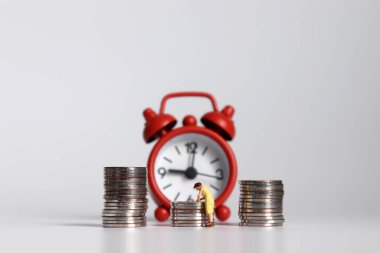 Minyatür bir kadın, çalar saatin önünde bir yığın bozuk parayla..