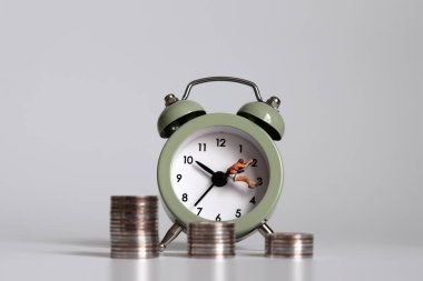 Çalar saati ve bozuk parası olan minyatür bir insan. Çalışma saatleri ve gelir eşitsizliği kavramı.