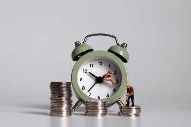 Çalışma saatleri ve gelir eşitsizliği kavramı. Çalar saati ve bozuk parası olan minyatür bir insan..