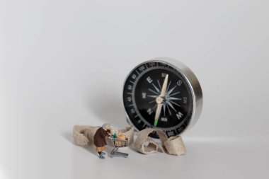 Fakir yaşlılık kavramı. Elinde alışveriş arabası ve pusulası olan minyatür bir ihtiyar..