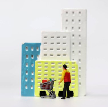 Minyatür bir evin önünde alışveriş arabası taşıyan minyatür teslimat şoförü..