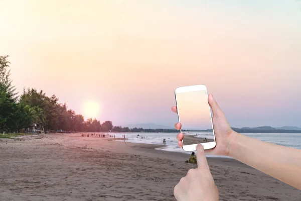 hand holding mobile smart phone with front the beach and sky  background