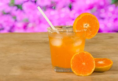 Bir bardak portakal suyu ve ahşap masada taze portakal, pembe bokeh arka plan.