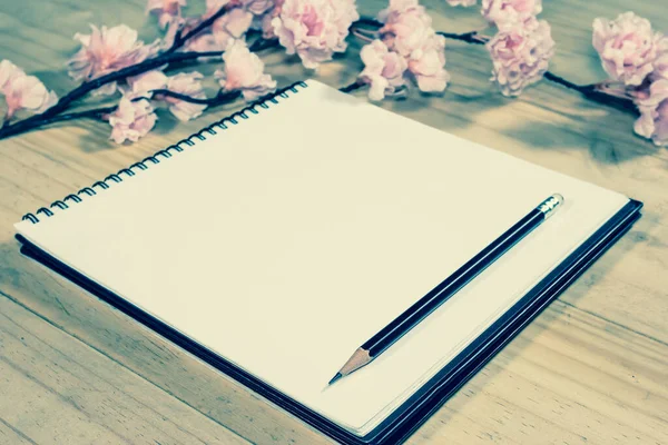 open note book with pink sakura flowers on wooden background,filter effect.